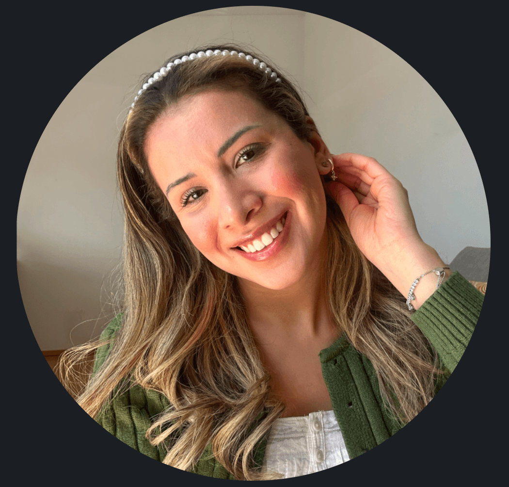 Lächelnde Frau mit langen blonden Haaren, Perlen-Haarreif und grünem Cardigan berührt ihr Ohr.
